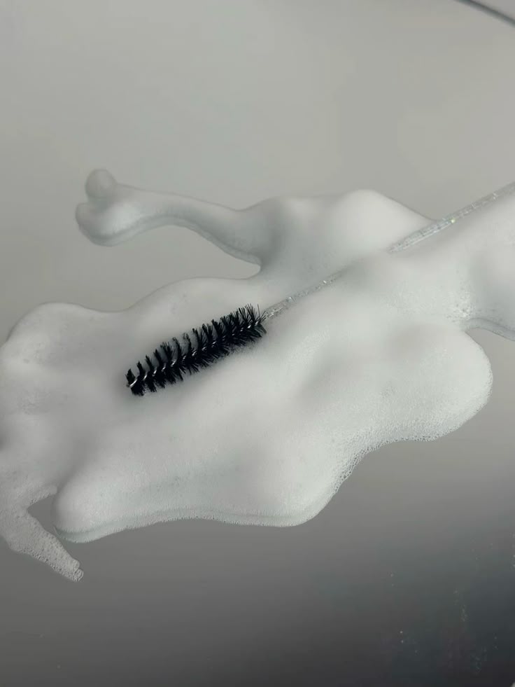 Black lash spoolie resting on white lash shampoo foam
